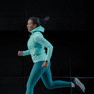 Woman running in teal athletic wear against a black background