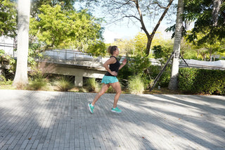 Woman running on a paved path in a park with trees and greenery.